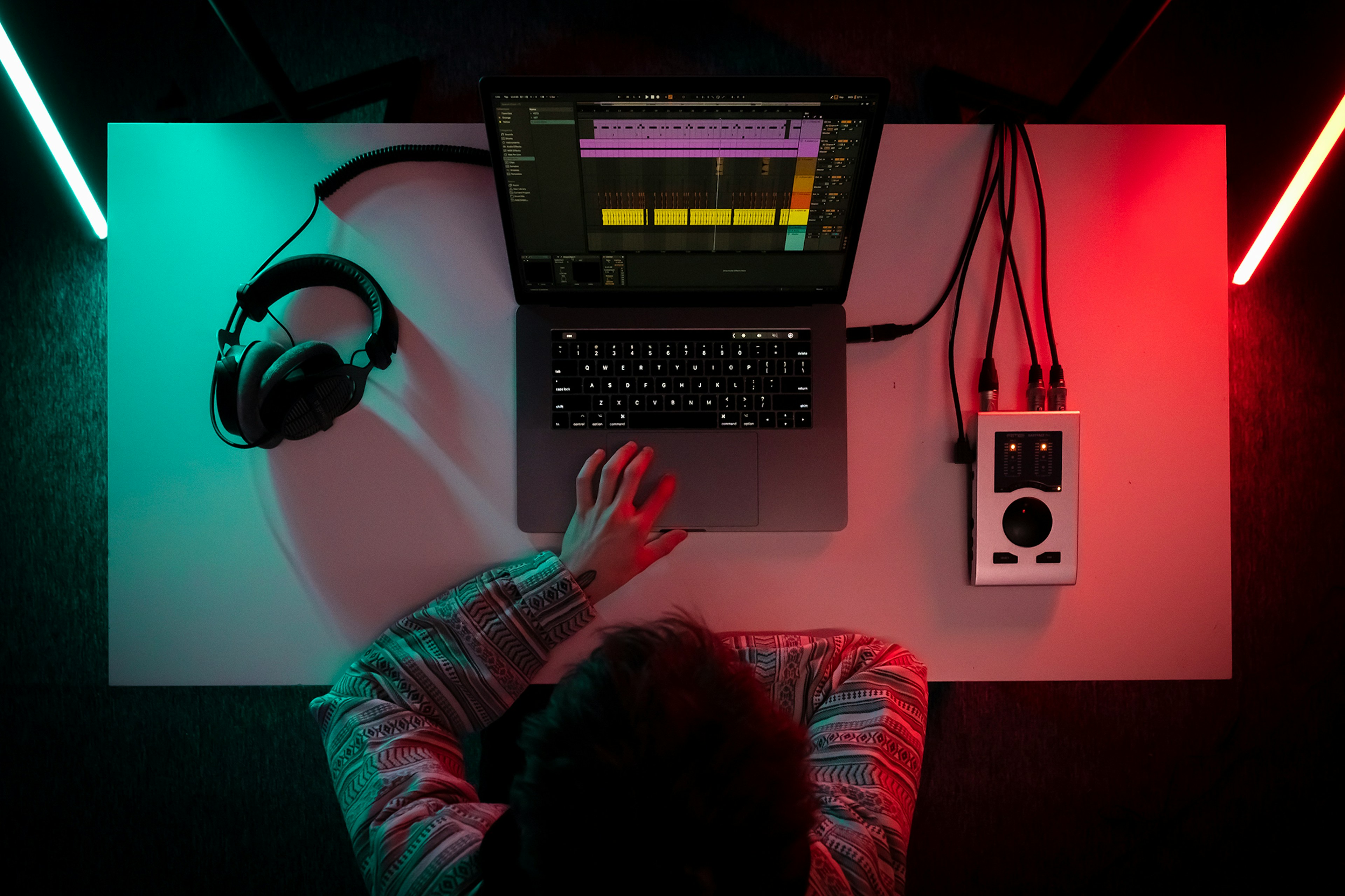 Music producer working on laptop with professional audio setup in colorful lighting