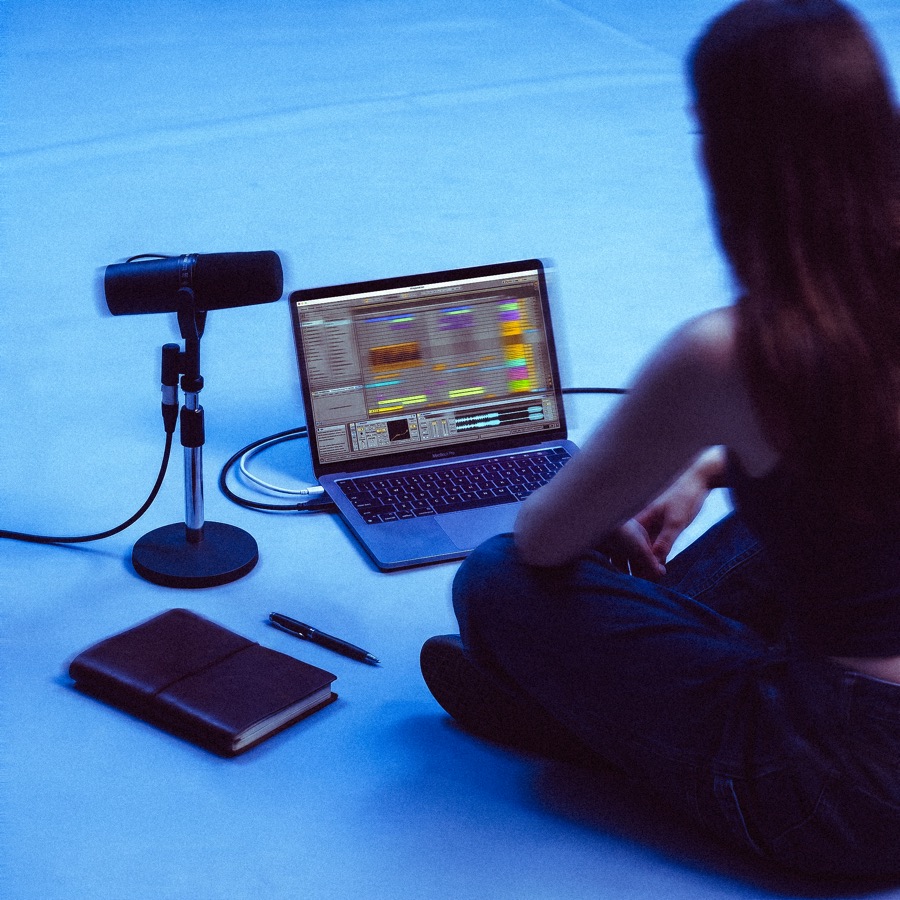 Student recording vocals into a studio microphone beside a laptop